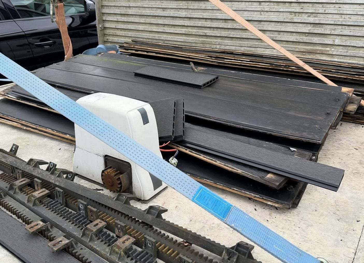 White sliding gate operator with its drive gear showing, set on a truck bed beside lengths of gear rack