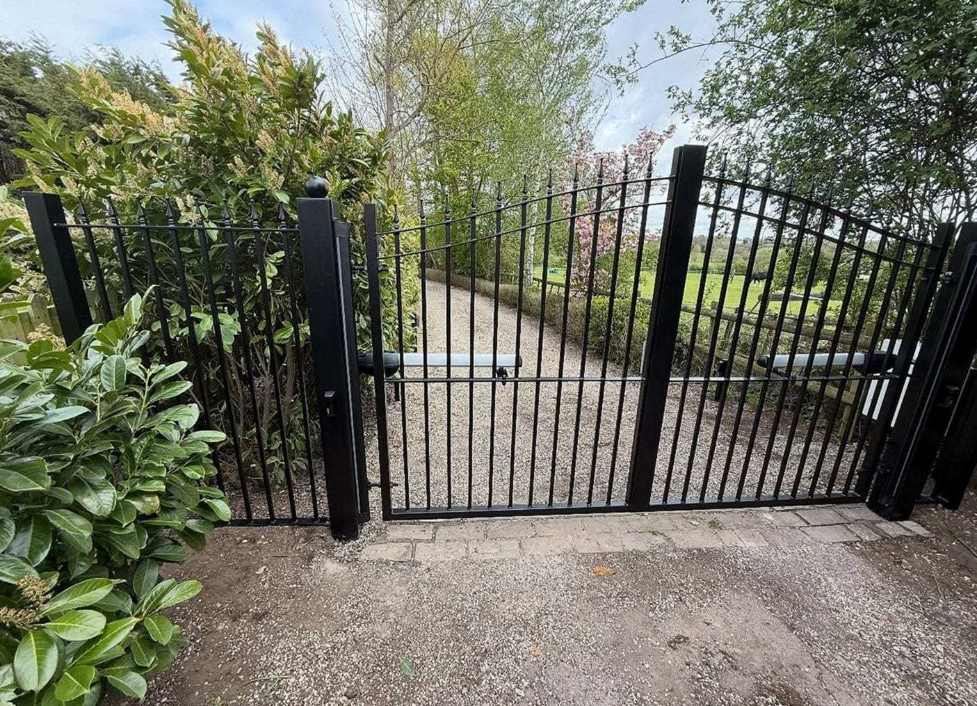 Black metal double swing gates with an arched top and a matching walk-through gate beside a garden path